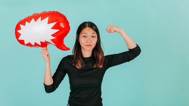 Mujer asiática con globo de discurso que muestra los músculos