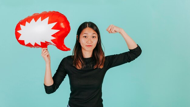 Mujer asiática con globo de discurso que muestra los músculos