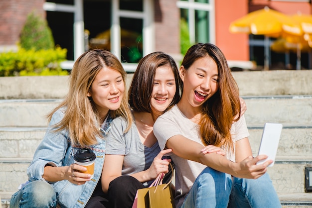 Mujer asiática hermosa atractiva que usa un smartphone mientras que hace compras en la ciudad