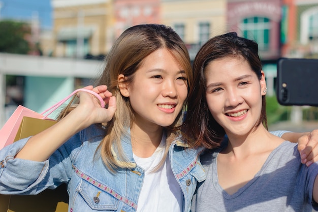 Mujer asiática hermosa atractiva que usa un smartphone mientras que hace compras en la ciudad