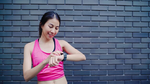 Mujer asiática hermosa hermosa sana del atleta que fija y que comprueba el progreso que mira el monitor del ritmo cardíaco