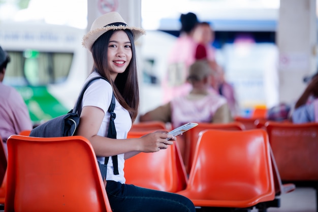 Mujer asiática hermosa que sonríe con el mapa y el bolso en la estación de autobuses