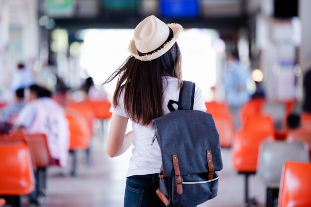 Mujer asiática hermosa que sonríe con el mapa y el bolso en la estación de autobuses