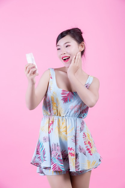 Mujer asiática hermosa que sostiene una botella de producto en un fondo rosado.