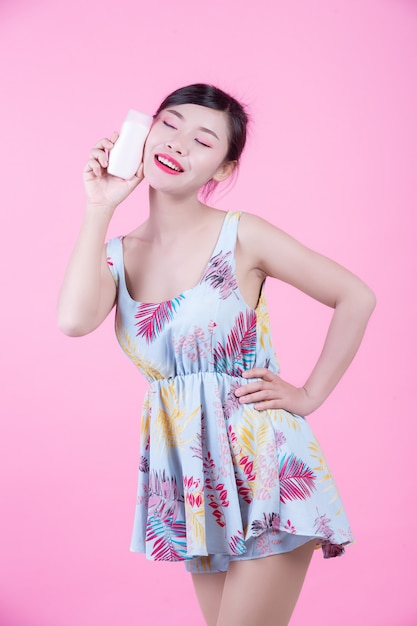 Mujer asiática hermosa que sostiene una botella de producto en un fondo rosado.