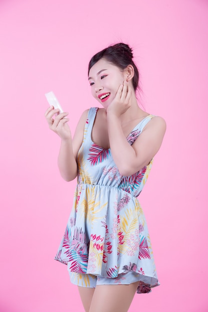 Mujer asiática hermosa que sostiene una botella de producto en un fondo rosado.