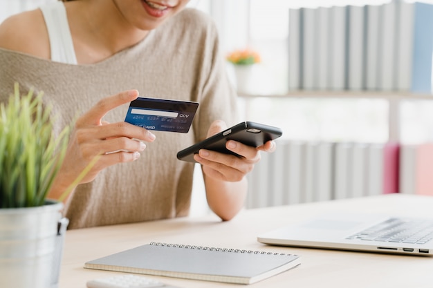 Mujer asiática hermosa que usa el teléfono inteligente que compra compras en línea