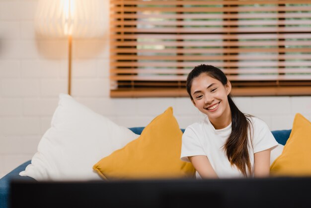 Mujer asiática joven del adolescente que ve la TV en casa, mentira feliz de la sensación femenina en el sofá en sala de estar.