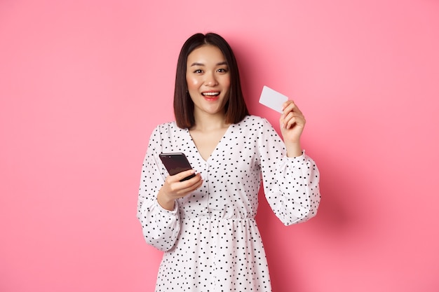 Mujer asiática joven atractiva orden en línea con tarjeta de crédito y teléfono móvil haciendo compra de internet ...