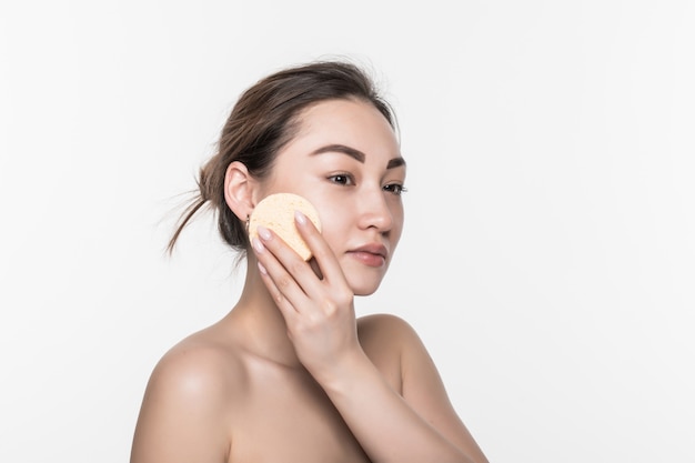 Mujer asiática joven de la belleza bonita que limpia su cara con el cojín de algodón sobre blanco aislado en la pared blanca. Concepto de cosmética y piel sana.