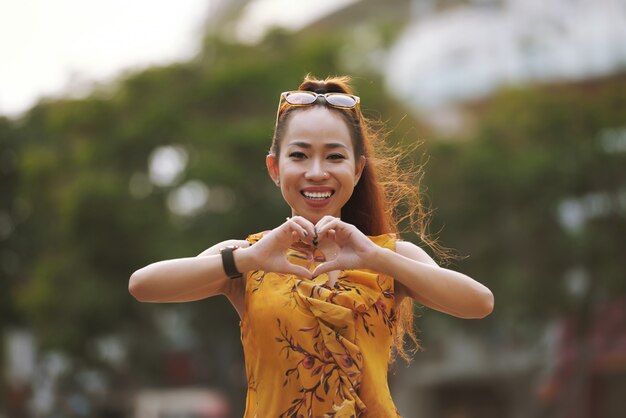 Mujer asiática joven elegante sonriente que muestra gesto del corazón