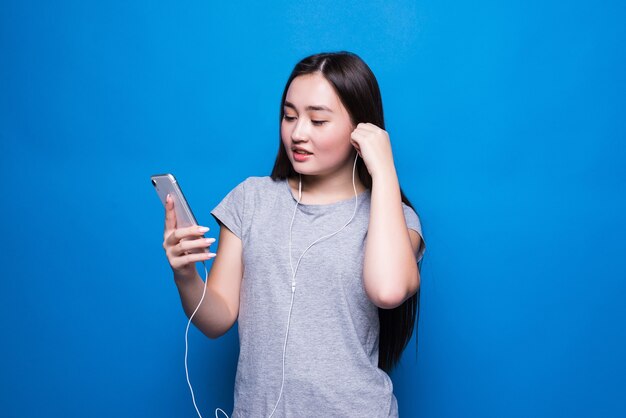 Mujer asiática joven escuchando música con auriculares rojos en la pared azul transparente. Entretenimiento, aplicación de música, vapor en línea