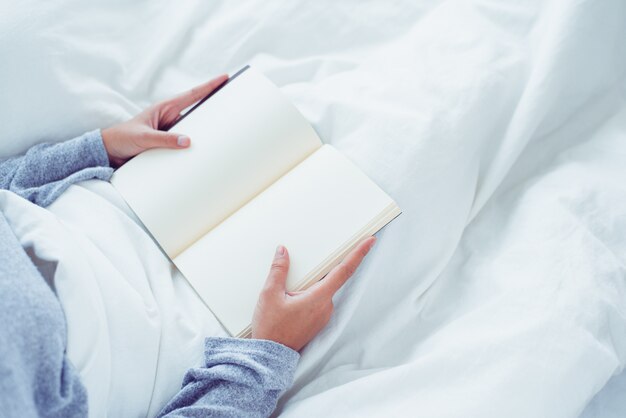 Mujer asiática joven feliz de la forma de vida que disfruta de mentir en el placer del libro de lectura de la cama en la ropa casual