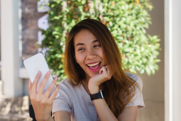 Mujer asiática joven feliz hermosa atractiva que toma un selfie usando un teléfono elegante en el café