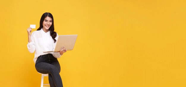 Mujer asiática joven feliz mostrando tarjeta de crédito y usando compras en línea de computadora