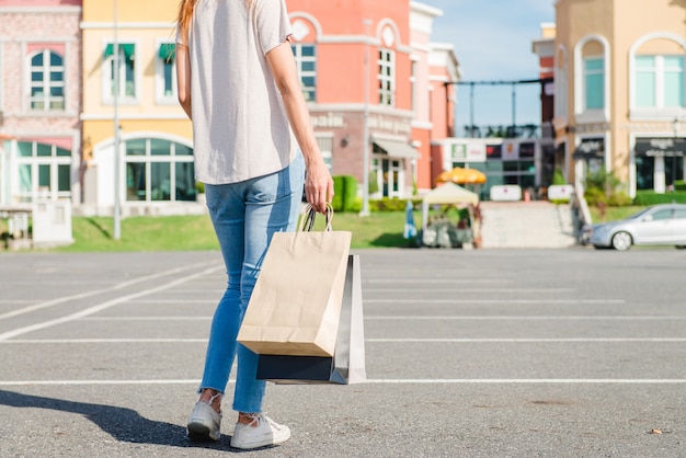 Mujer asiática joven feliz que hace compras un mercado al aire libre con un fondo de edificios en colores pastel