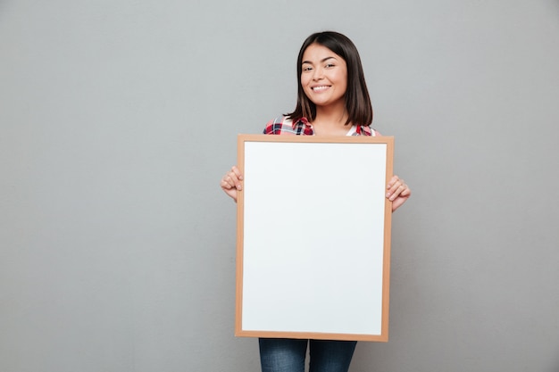 Mujer asiática joven feliz que lleva a cabo el copyspace en blanco.