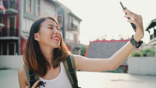 Mujer asiática joven hermosa alegre alegre del blogger del backpacker que usa el smartphone que toma el selfie
