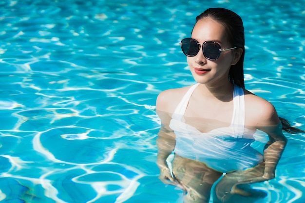 La mujer asiática joven hermosa feliz y la sonrisa en la piscina para relajan viaje y vacaciones