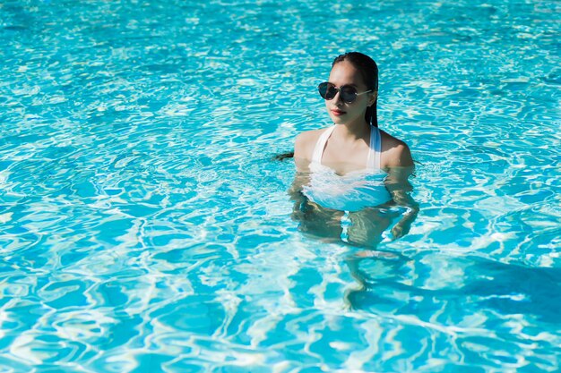 La mujer asiática joven hermosa feliz y la sonrisa en la piscina para relajan viaje y vacaciones