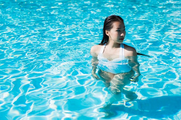 La mujer asiática joven hermosa feliz y la sonrisa en la piscina para relajan viaje y vacaciones