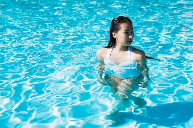 La mujer asiática joven hermosa feliz y la sonrisa en la piscina para relajan viaje y vacaciones