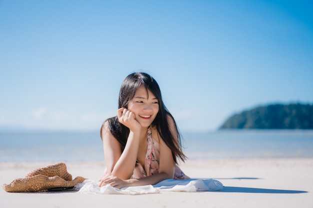 La mujer asiática joven hermosa que miente en feliz de la playa se relaja cerca del mar.