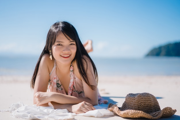 La mujer asiática joven hermosa que miente en feliz de la playa se relaja cerca del mar.