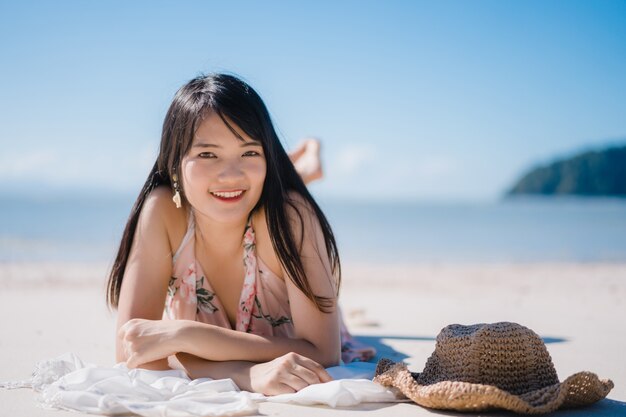 La mujer asiática joven hermosa que miente en feliz de la playa se relaja cerca del mar.