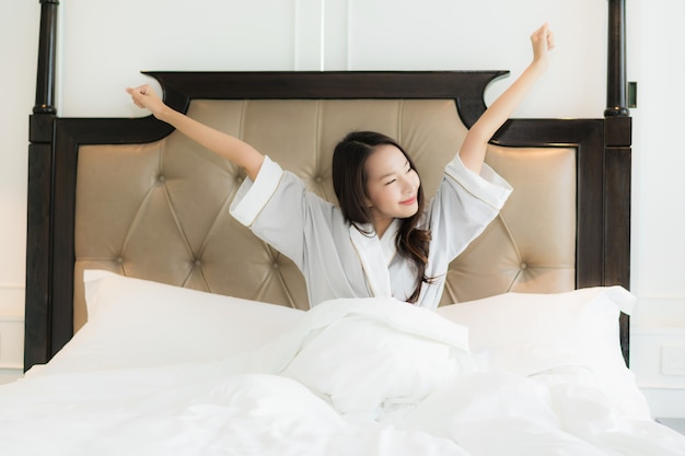 La mujer asiática joven hermosa del retrato despierta con feliz y sonríe en cama en interior del dormitorio