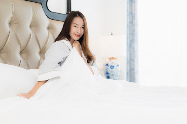 La mujer asiática joven hermosa del retrato despierta con feliz y sonríe en cama en interior del dormitorio