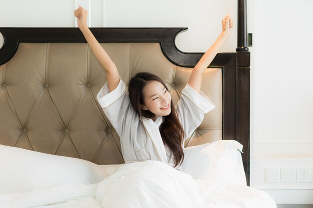 La mujer asiática joven hermosa del retrato despierta con feliz y sonríe en cama en interior del dormitorio