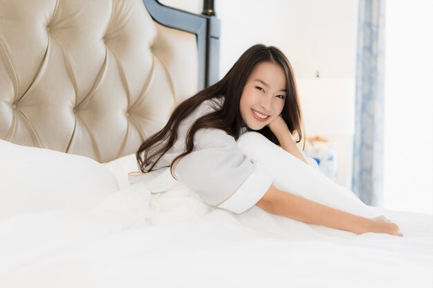 La mujer asiática joven hermosa del retrato despierta con feliz y sonríe en cama en interior del dormitorio