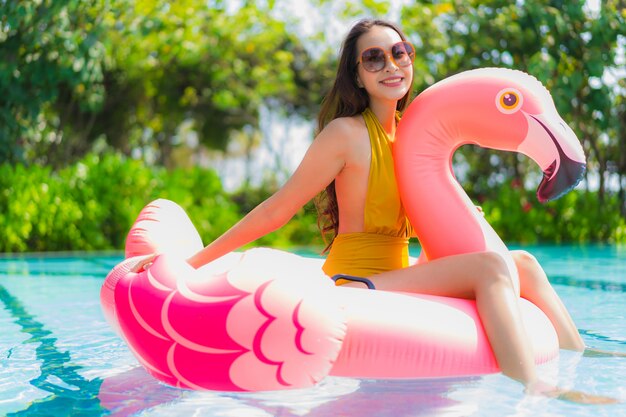 Mujer asiática joven hermosa del retrato en el flotador inflable del flamenco en piscina en el centro turístico del hotel