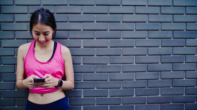 Mujer asiática joven hermosa sana del atleta que usa el smartphone para comprobar medios de comunicación social