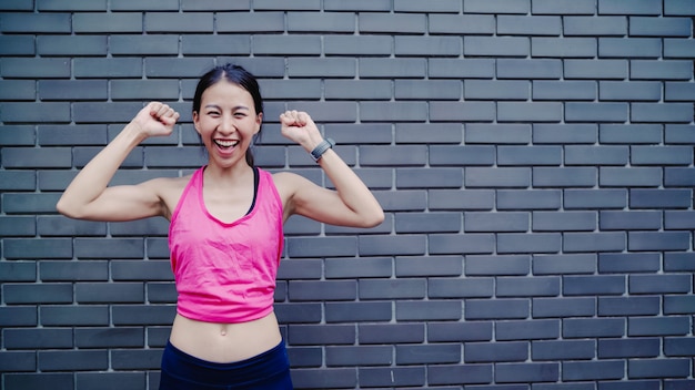 Mujer asiática joven hermosa sana del corredor que siente la sonrisa feliz y que mira a la cámara después de correr