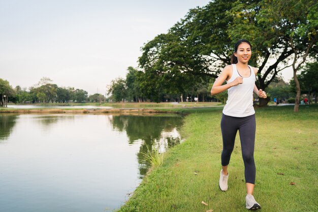 Mujer asiática joven hermosa sana del corredor en la ropa de los deportes que corre y que activa