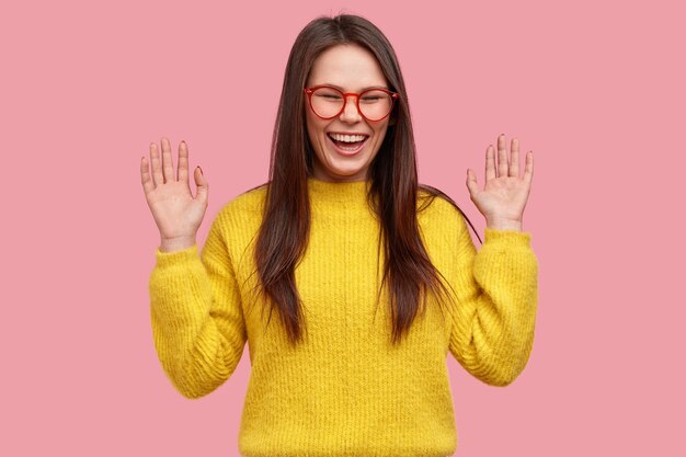 Mujer asiática joven positiva con expresión de alegría, muestra las palmas, se ríe ante una broma divertida