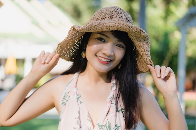 La mujer asiática joven que se sienta en banco se relaja en la playa, feliz femenino hermoso se relaja cerca del mar.