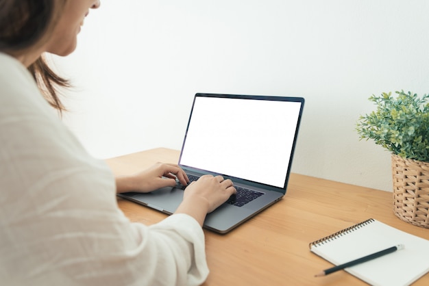 Mujer asiática joven que trabaja usando y escribiendo en la computadora portátil con mock up pantalla en blanco en blanco