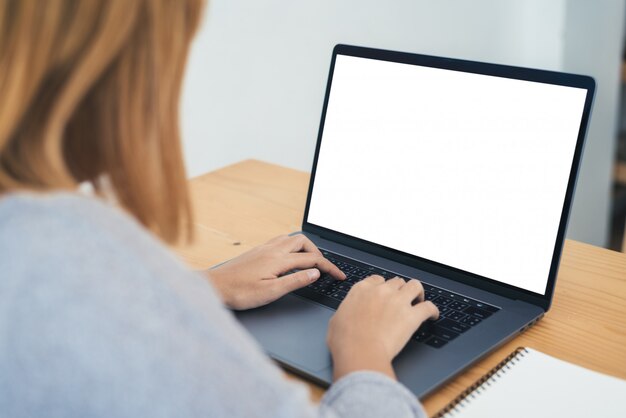 Mujer asiática joven que trabaja usando y escribiendo en la computadora portátil con mock up pantalla en blanco en blanco