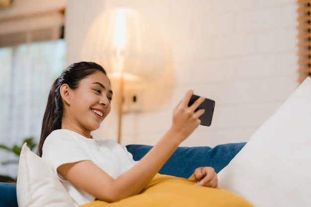 Mujer asiática joven que usa el smartphone que comprueba medios sociales que sienten la sonrisa feliz