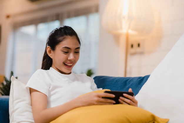 Mujer asiática joven que usa el smartphone que comprueba medios sociales que sienten la sonrisa feliz