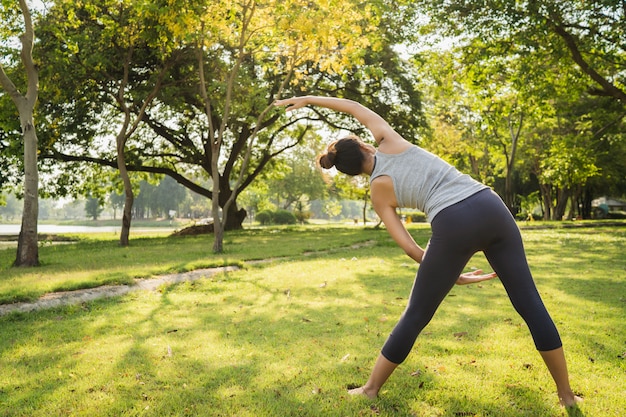 La mujer asiática joven sana del corredor calienta el cuerpo que estira antes de ejercicio y de yoga