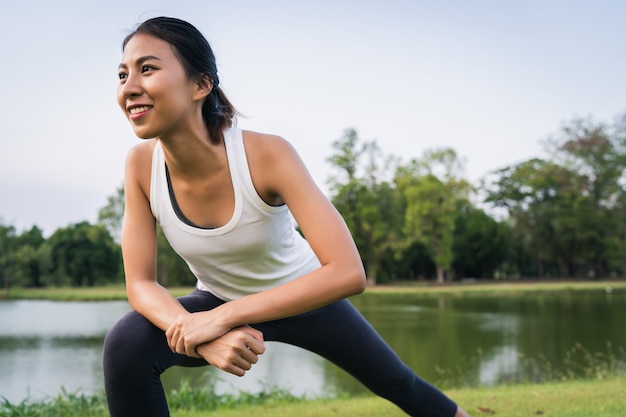 La mujer asiática joven sana del corredor calienta el cuerpo que estira antes de ejercicio y de yoga