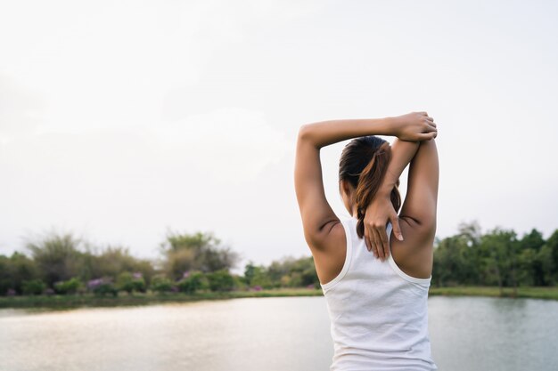 La mujer asiática joven sana del corredor calienta el cuerpo que estira antes de ejercicio y de yoga