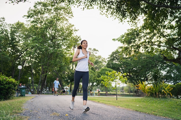 Mujer asiática joven sana del corredor en la ropa de los deportes que corre y que activa en la acera