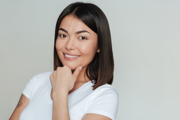 Mujer asiática joven sonriente aislada sobre la pared gris.