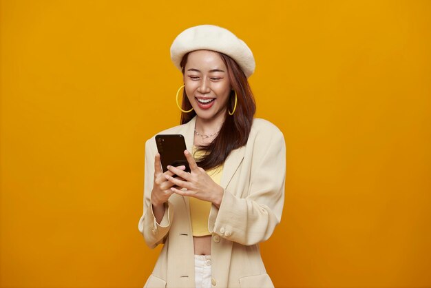 Mujer asiática joven sonriente feliz que usa el teléfono móvil aislado en y