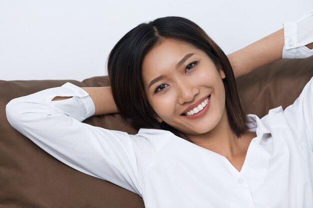 Mujer asiática joven sonriente que miente en el amortiguador